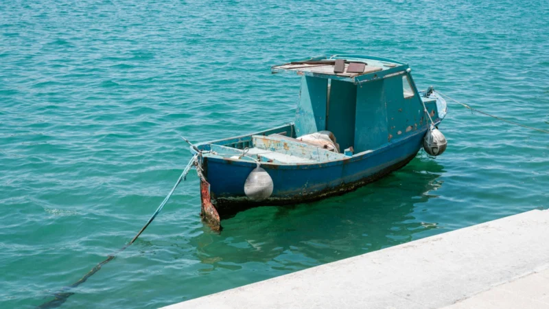 Petite barque de pêche bleue amarrée près d'un quai dans une eau turquoise (photo d'illustration)