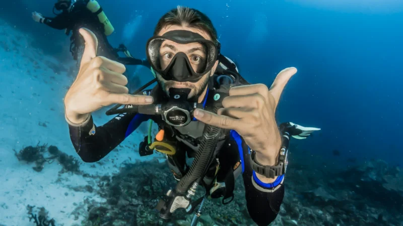 Plongeur en combinaison faisant un signe de la main sous l'eau
