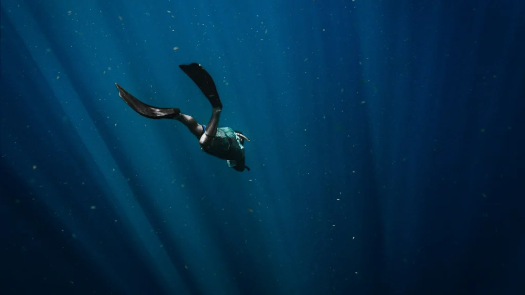 Plongeur en combinaison noire descendant dans une eau bleue profonde